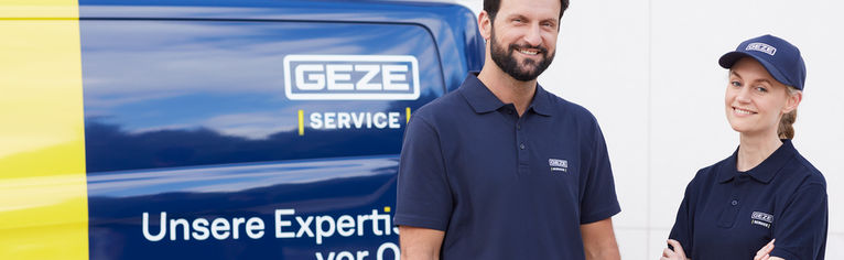 Two GEZE service employees in company clothing smile in front of a service vehicle.
